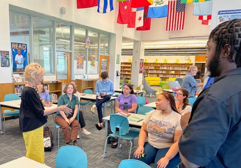 A blonde woman teaches adults in a school library.